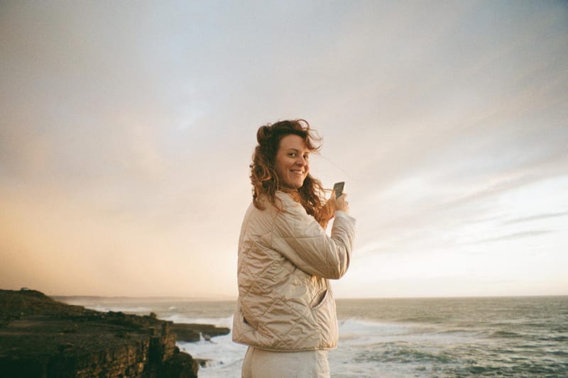 Woman holding her phone while walking by the coast