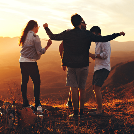 A group of friends standing on the top of a mountain at sunset.