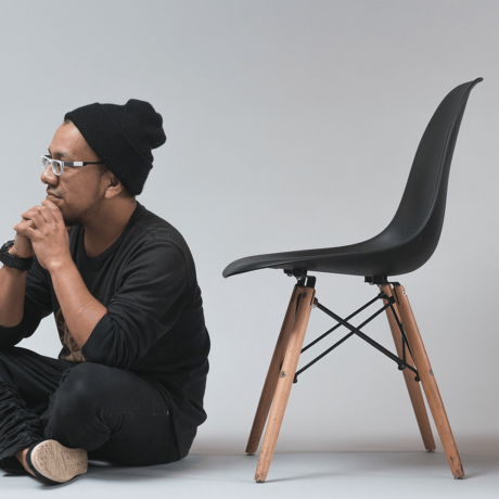 Man wearing all black sitting on the floor next to a black chair