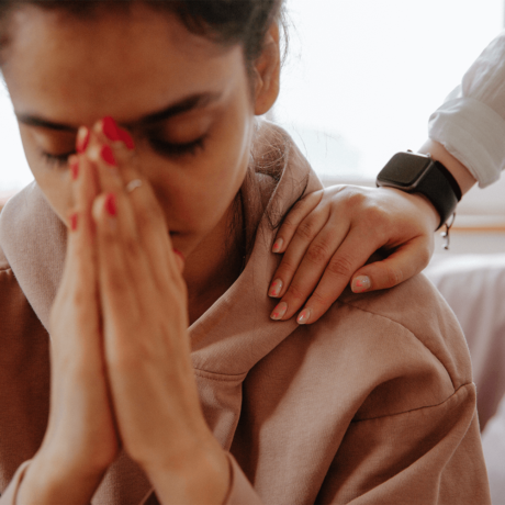 Woman holding her hands to her face while being comforted