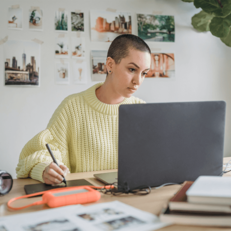 Woman with shaved head working on a laptop while sitting at her desk.