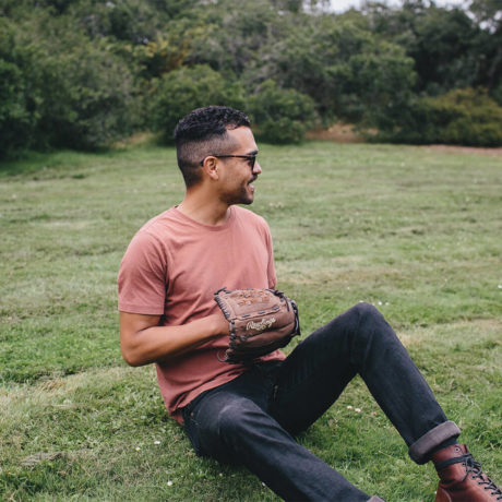Man sitting in the grass while smiling and holding a baseball mitt