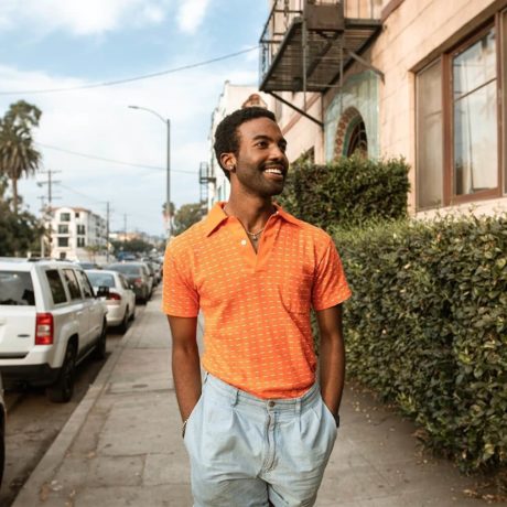 Smiling man wearing orange shirt walking on the sidewalk