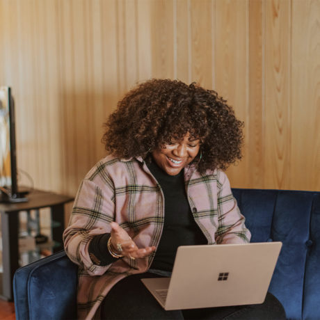 woman sitting on a couch working on her laptop and smiling