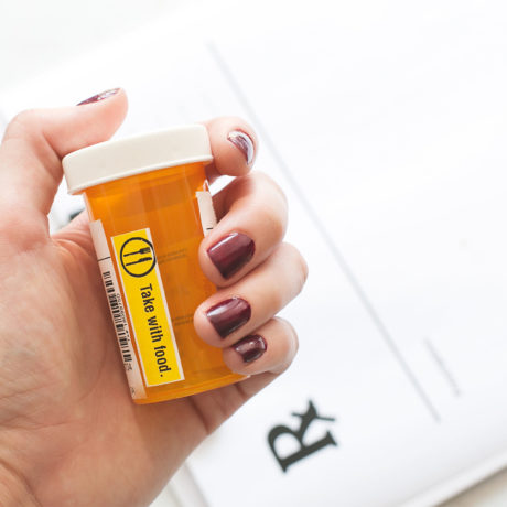 Woman holding a pill container with the words take with food on the side