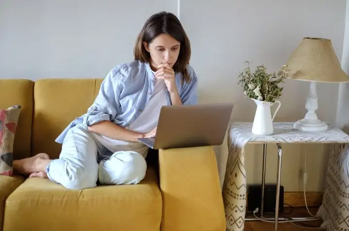 woman sitting on a couch looking at a laptop screen